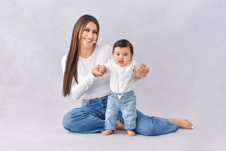 a woman sitting on the floor with a baby in her lap and pointing at something