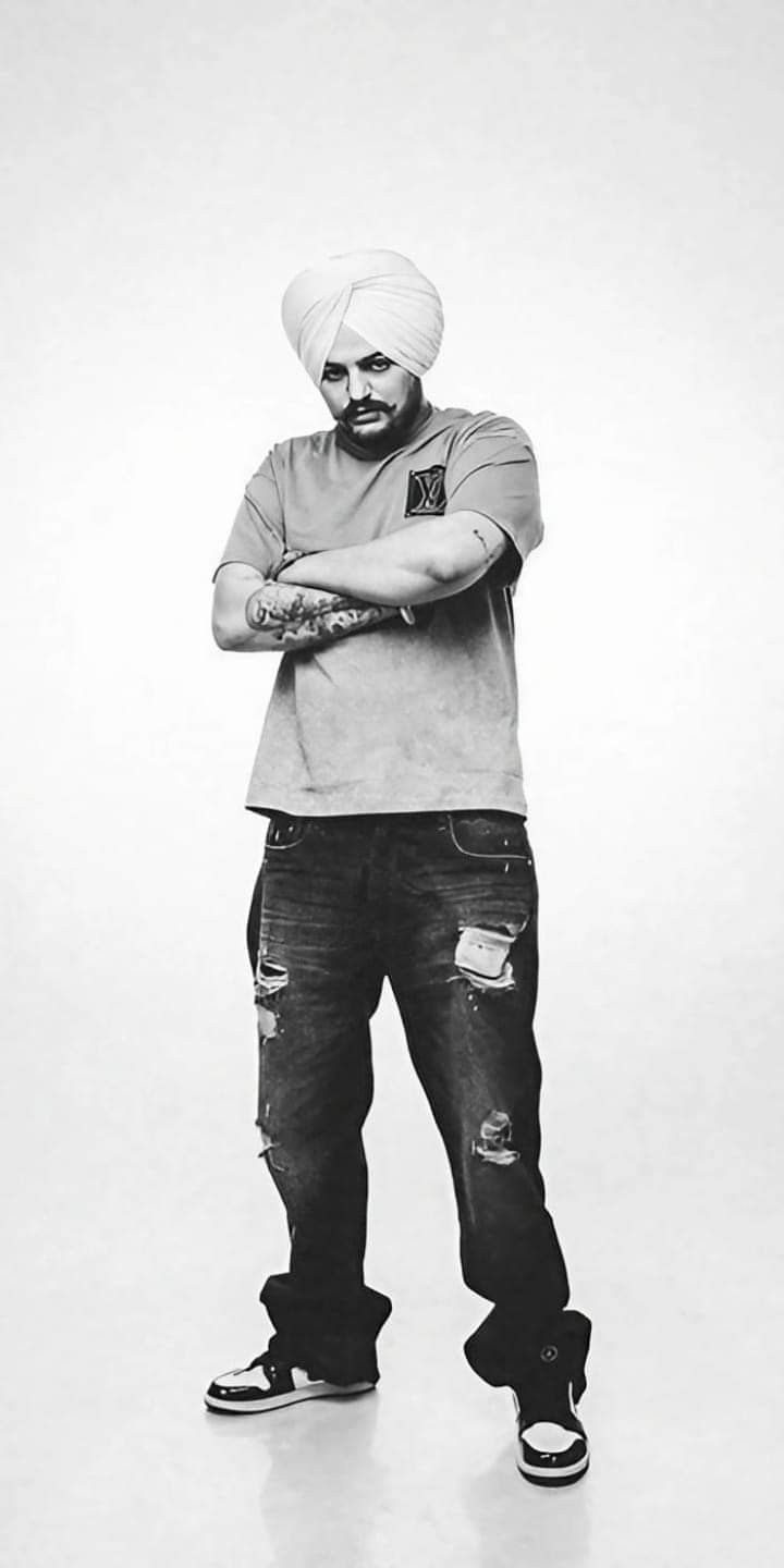 a man with a turban standing in front of a white background wearing ripped jeans