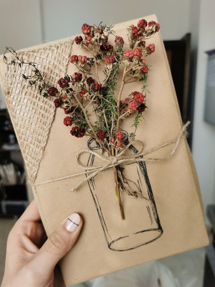 a person holding a card with dried flowers in a mason jar