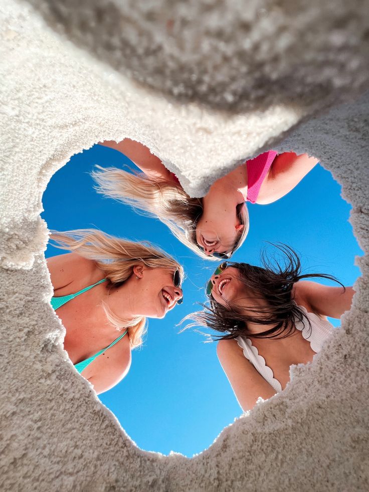 two women in bikinis are looking at each other through a hole in the sand