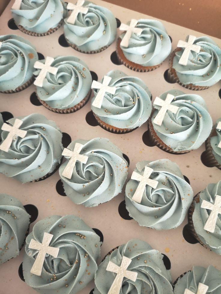 cupcakes with blue frosting and white crosses on them in a cardboard box