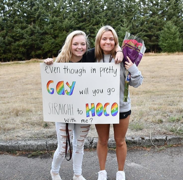 two girls holding up a sign that says gay will you go straight to hoco with me?