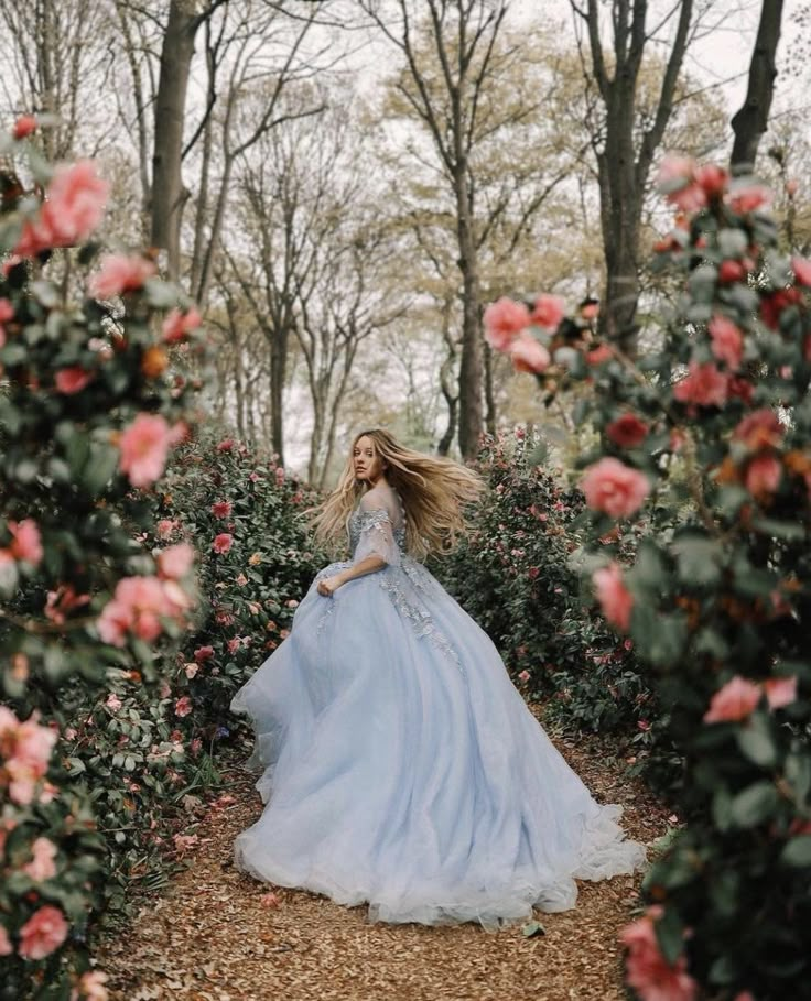 a woman in a blue dress is walking through some bushes and flowers with her hair blowing in the wind