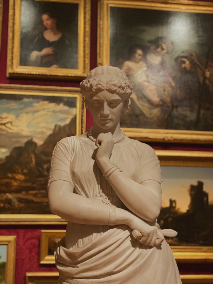 a statue of a woman in front of paintings on the wall with her hands clasped to her chin