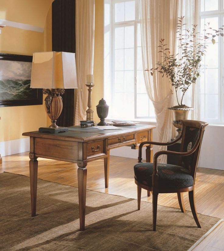 a room with a desk, chair and two lamps on the floor in front of large windows