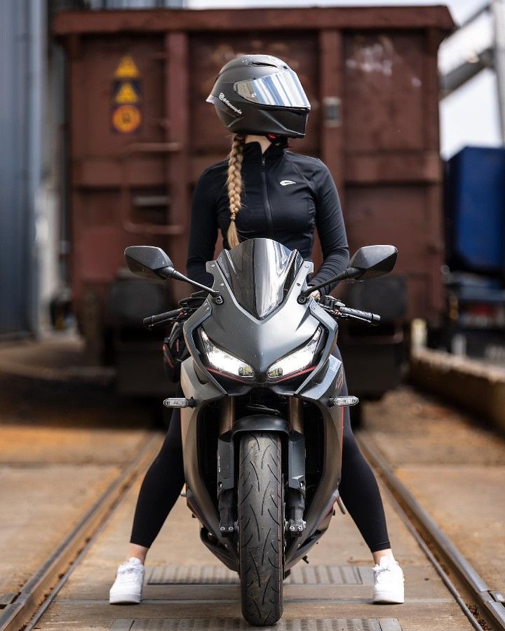 a woman sitting on top of a motorcycle next to a train track and wearing a helmet