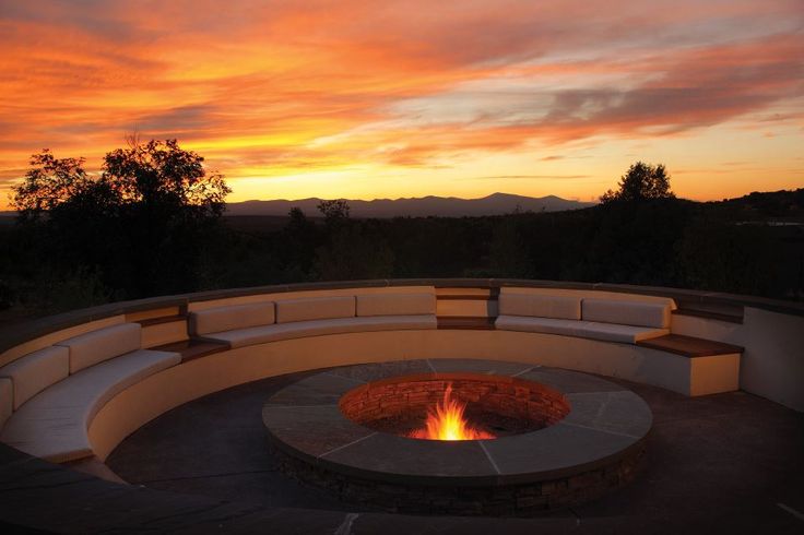 an outdoor fire pit with benches around it at sunset or dawn, overlooking the mountains