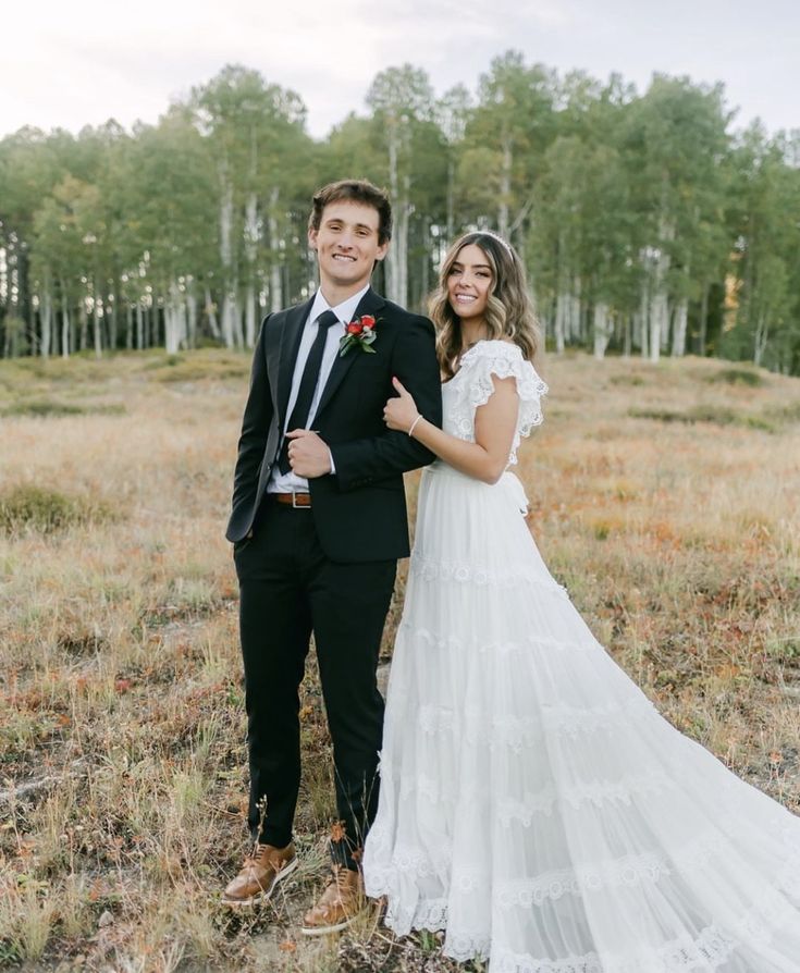 a bride and groom posing for a photo in an open field with trees behind them