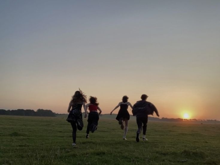 three girls running in a field at sunset