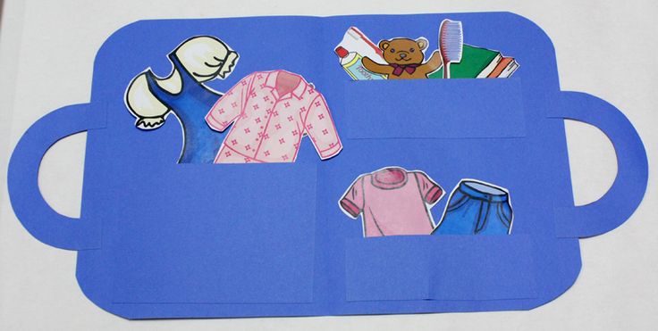 an open book with paper cut out of clothes and teddy bear on the top, sitting on a blue mat