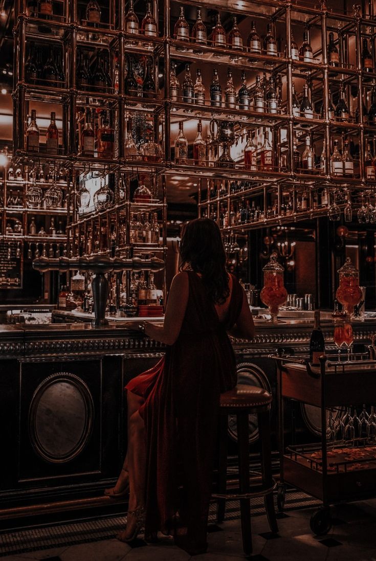 a woman sitting at a bar with lots of bottles on the wall