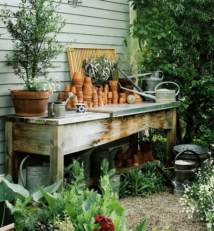 an outdoor garden with potted plants and pots on a table in front of a house