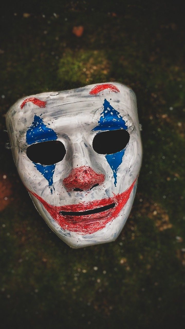 a white mask with blue and red painted on it's face sitting in the grass