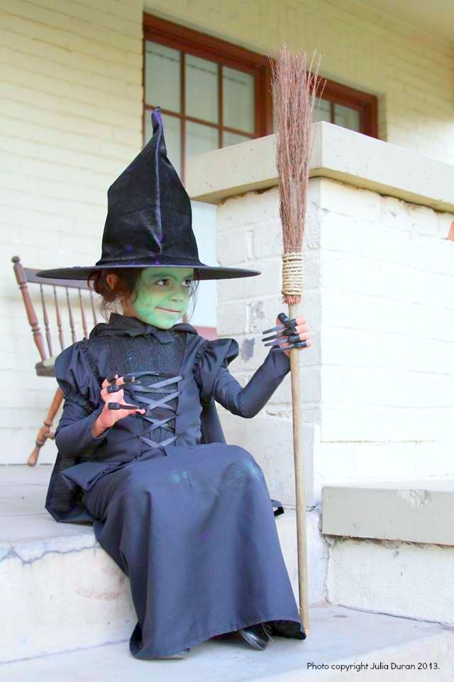 a woman dressed as a witch sitting on the steps with a broom in her hand