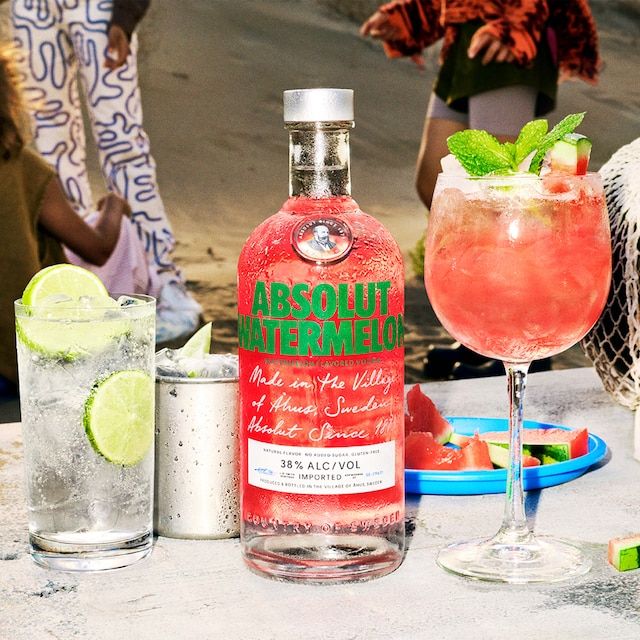 a bottle of absolut watermelon sitting next to two glasses with limes