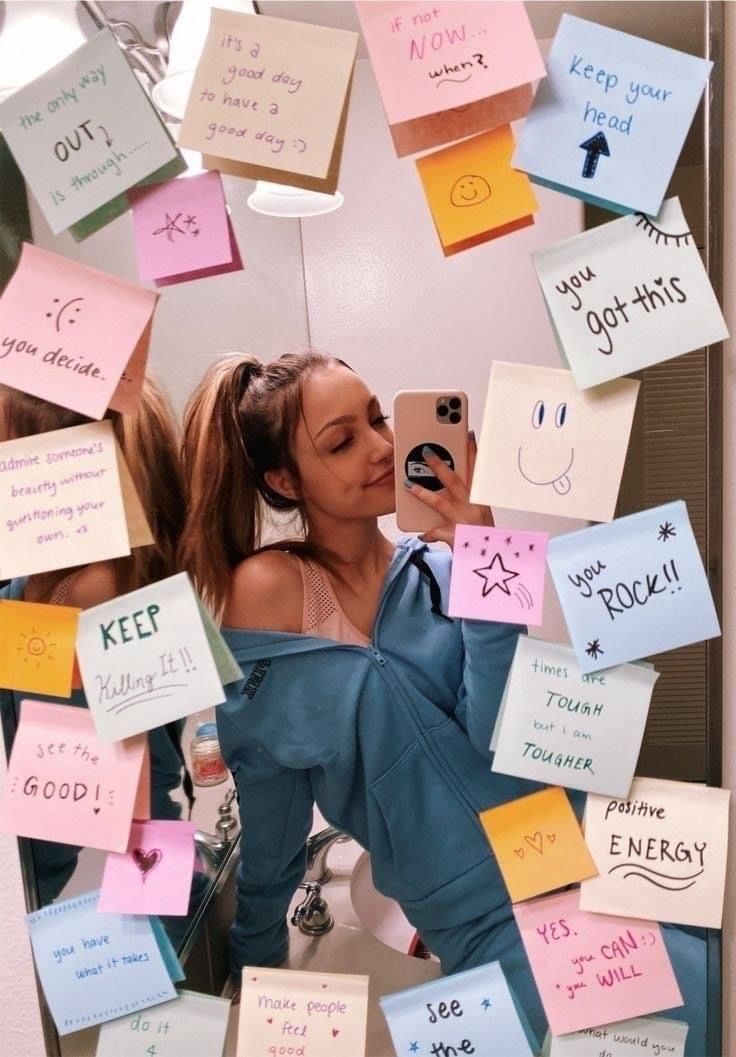 a woman taking a selfie in front of a mirror covered with post it notes