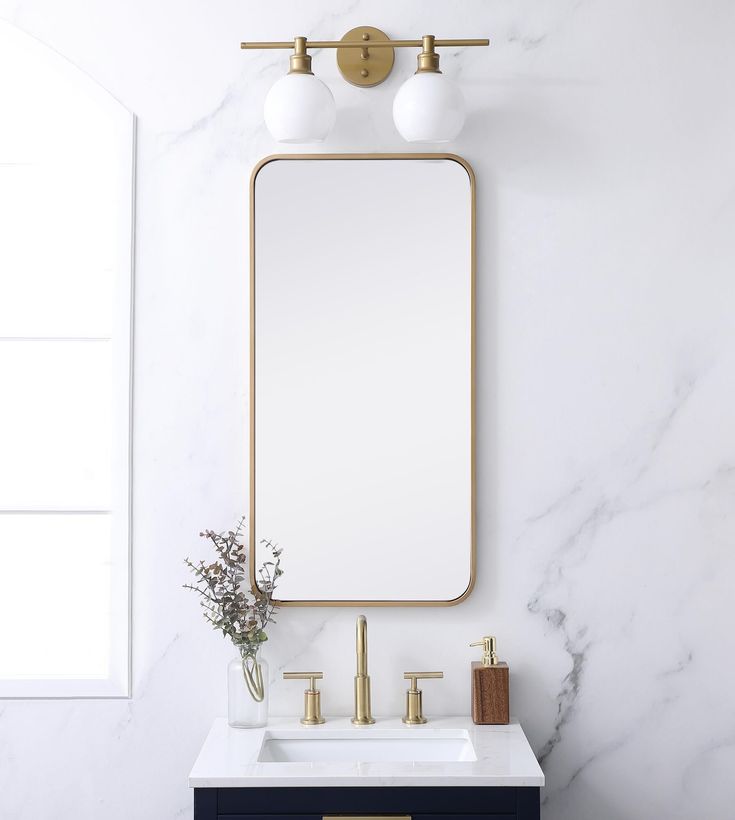 a bathroom with marble counter top and gold framed mirror on the wall, along with two brass faucets