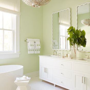 a bathroom with green walls and white fixtures, including a large mirror over the bathtub