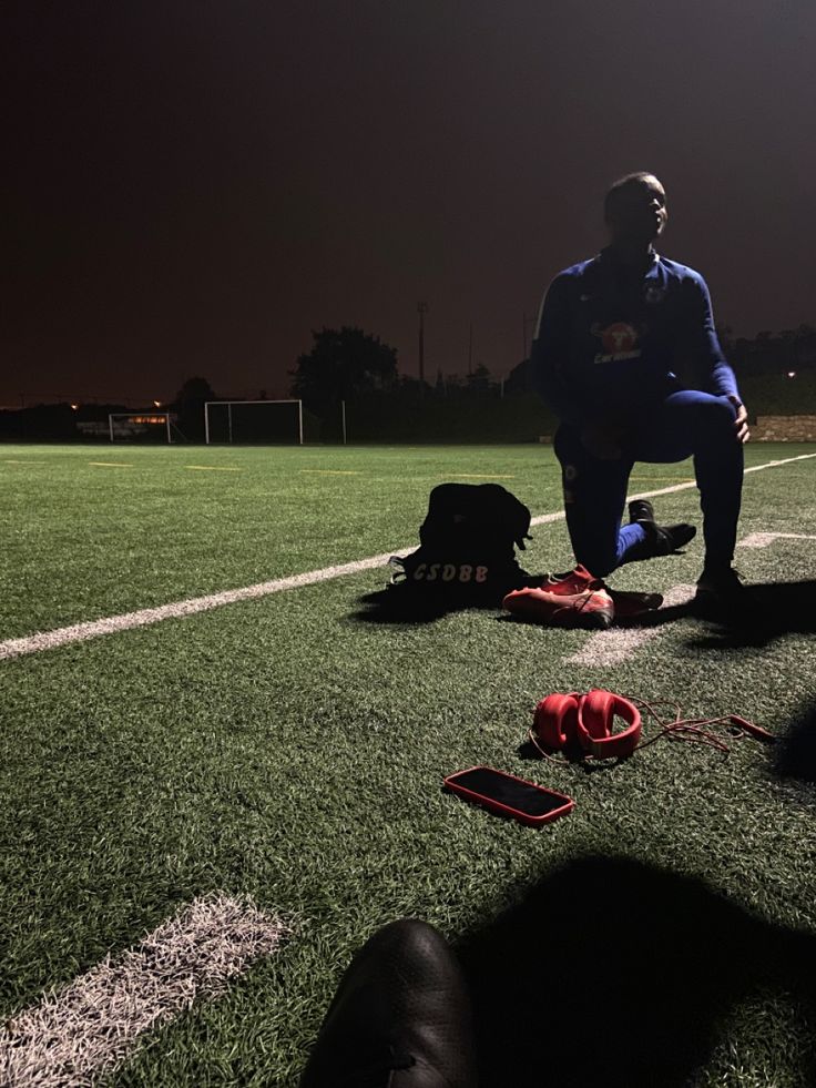 a man kneeling down on top of a soccer field next to a bag and shoes