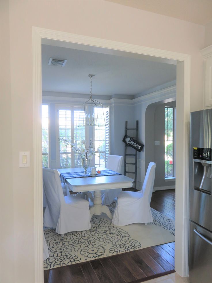 a dining room table with white chairs is seen through an open door to the kitchen