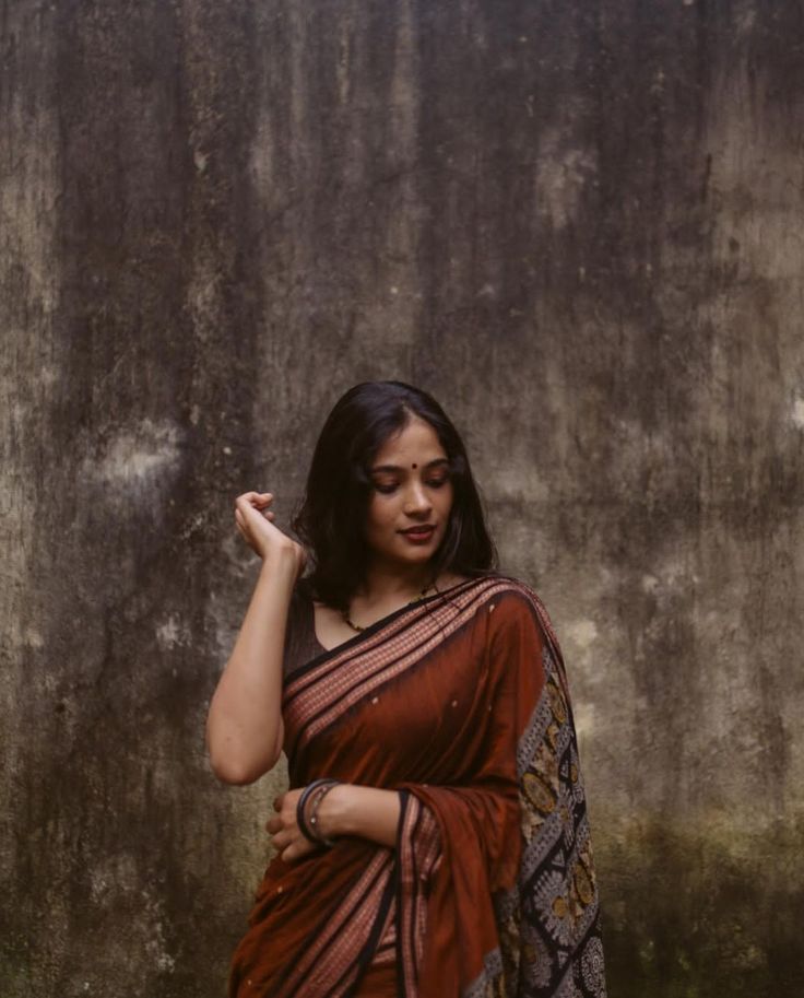 a woman standing in front of a wall wearing a red and black sari with an intricate design on it