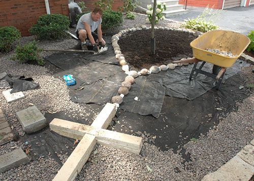 a man kneeling down next to a yellow wheelbarrow on top of a garden