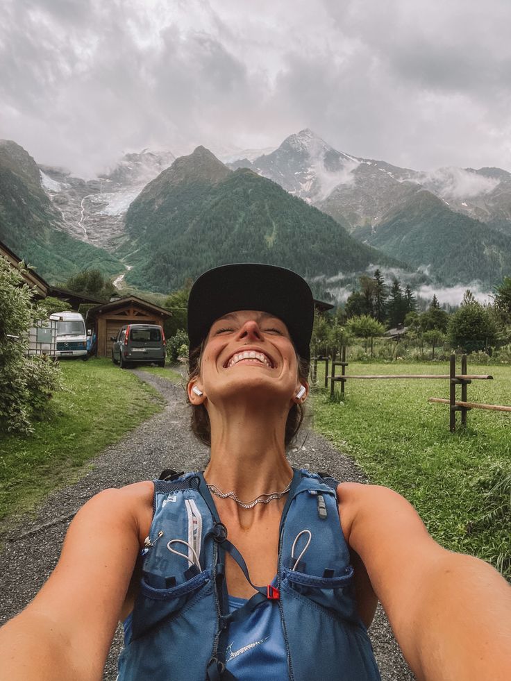 a woman is taking a selfie in front of some mountains and grass with her hands behind her head