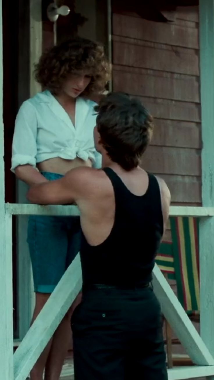 two women standing on the front porch of a house, one holding her arm around the other's shoulder