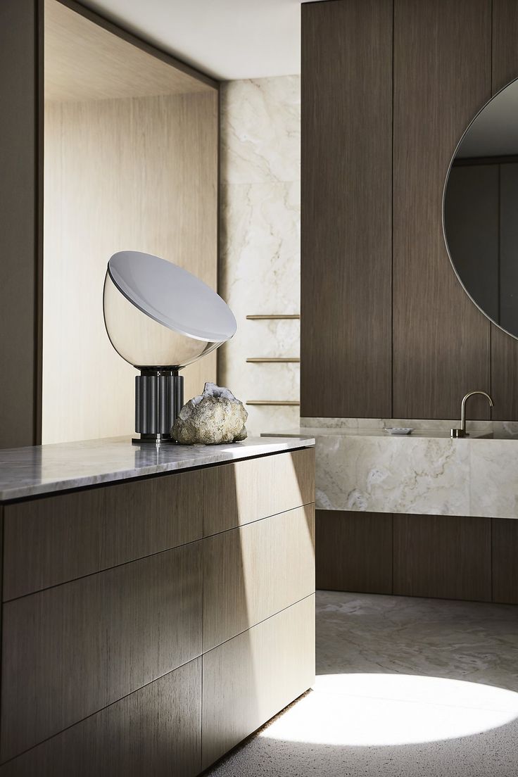 a modern kitchen with marble counter tops and wooden cabinetry, along with an oval mirror on the wall