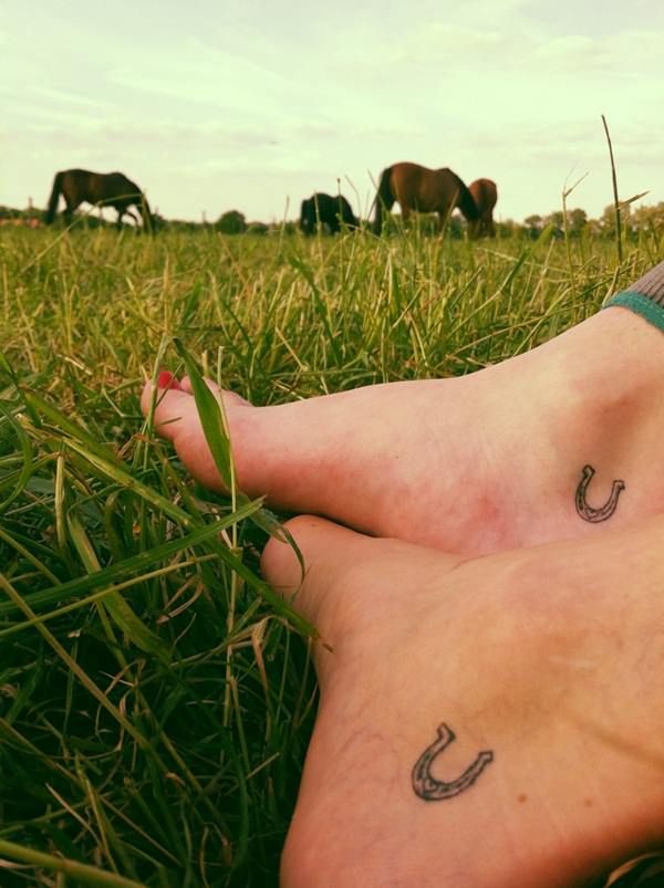 a person laying in the grass with their legs crossed and two horses grazing behind them