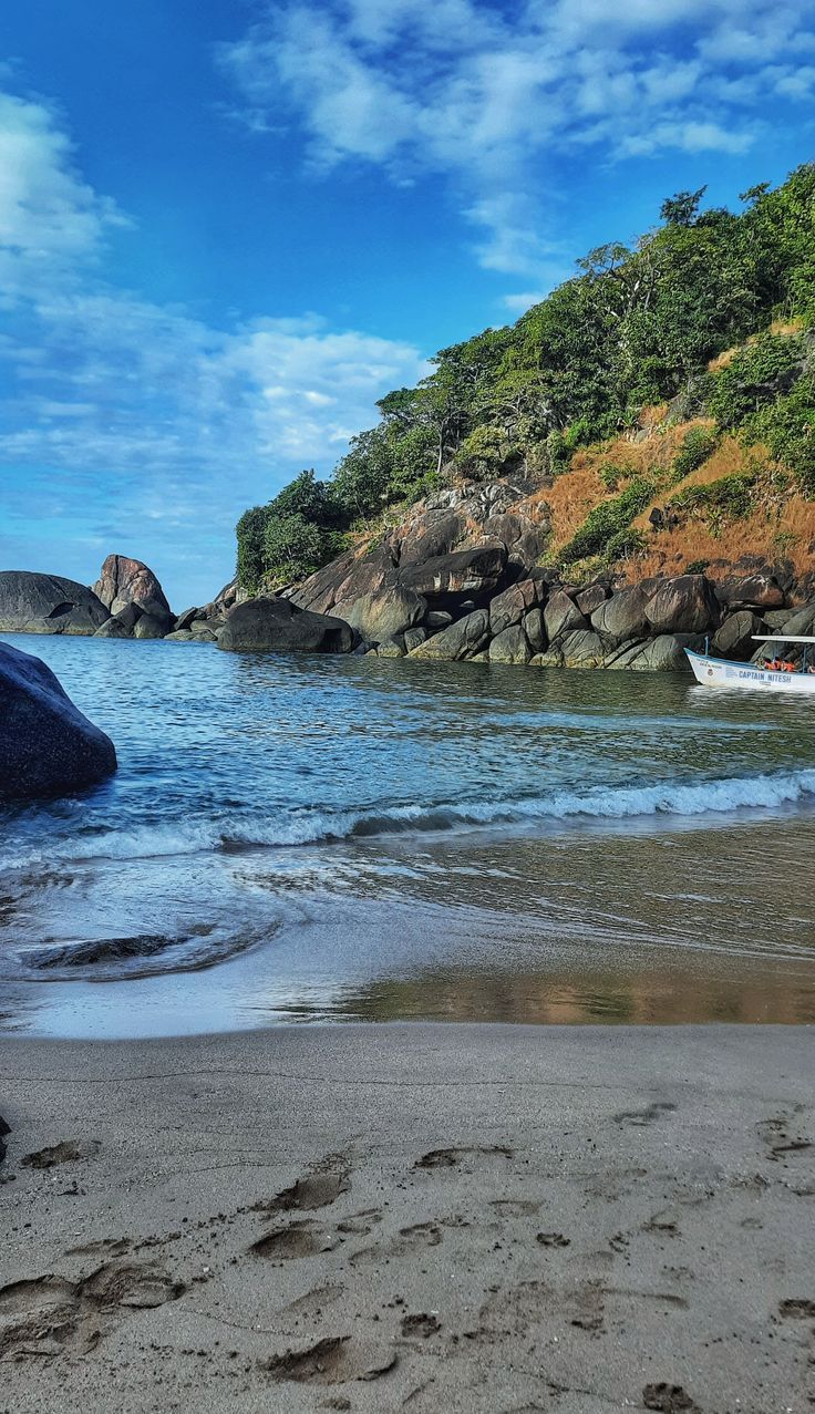 there is a boat that is in the water on the beach near some rocks and trees