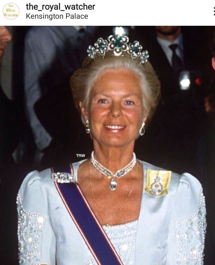 an older woman wearing a tiara and smiling at the camera with other people behind her