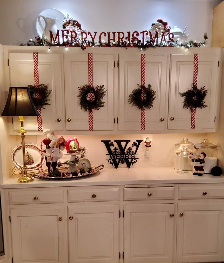 a christmas display with wreaths and decorations on top of the cabinets in a kitchen