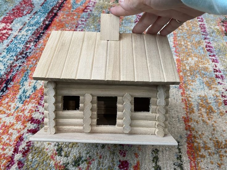 a person holding a wooden toy house on top of a rug