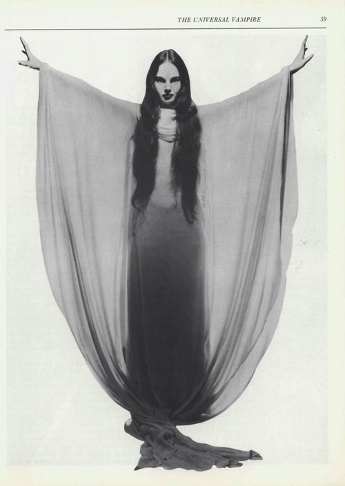 a woman with long black hair is standing in front of a white curtain and holding her arms out