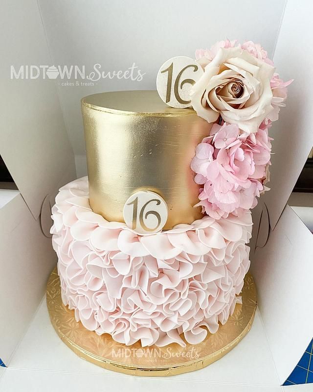 a gold and pink cake with flowers on top is in a cardboard box, ready to be eaten