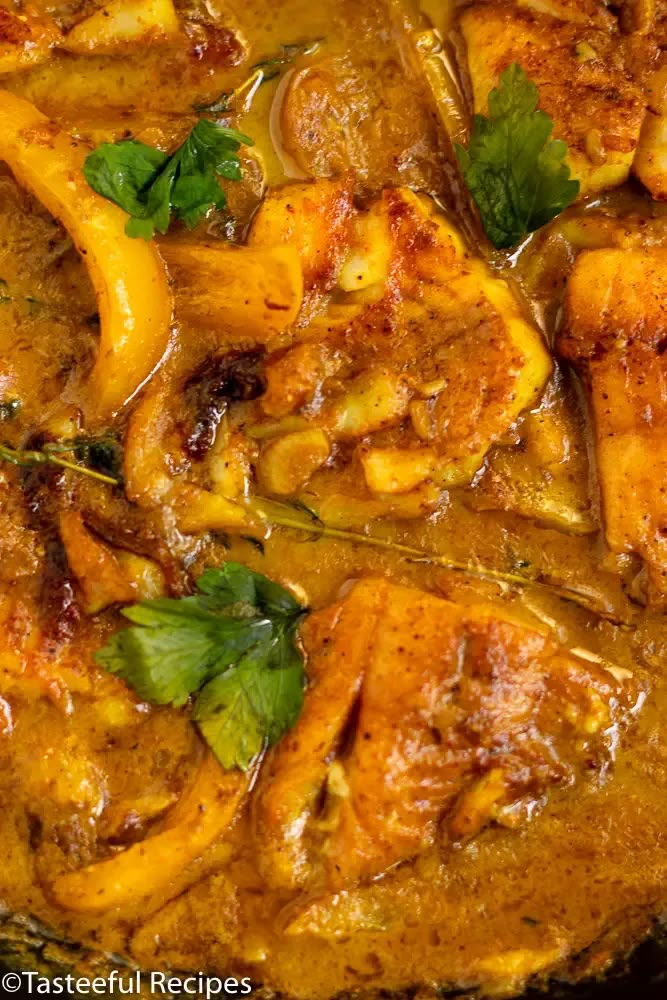 chicken curry in a pan with cilantro and coriant leaves on top