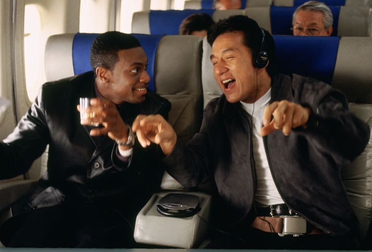 two men in suits sitting on an airplane and pointing at something off to the side