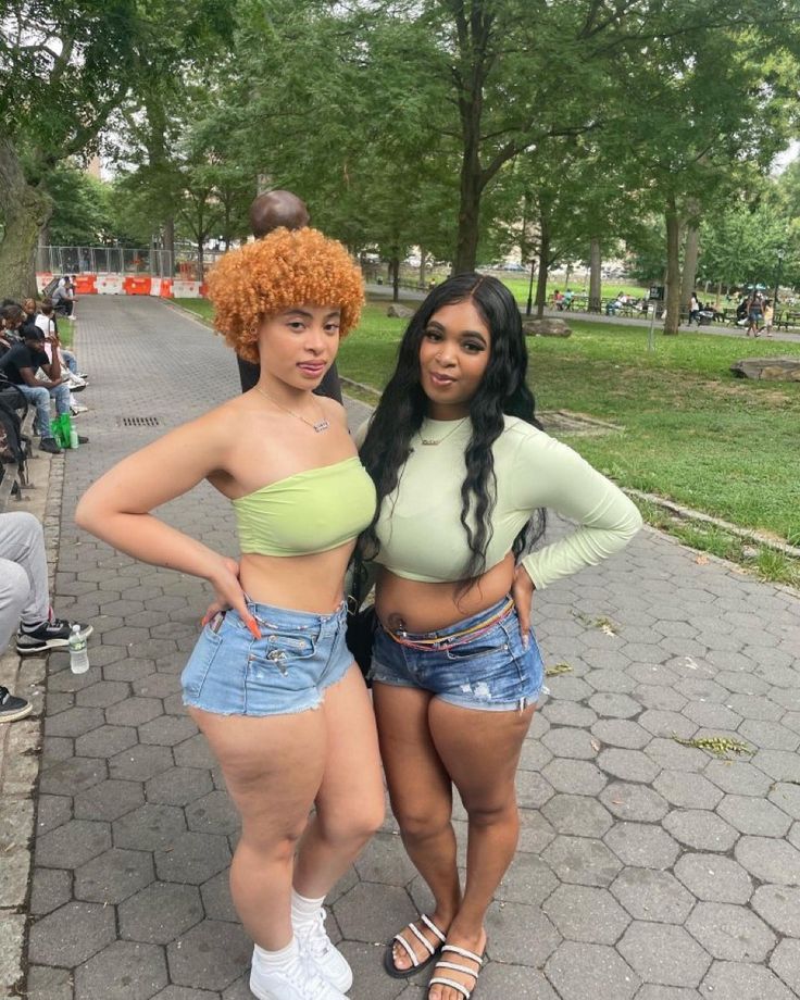 two women standing next to each other in shorts and cropped tops on the street