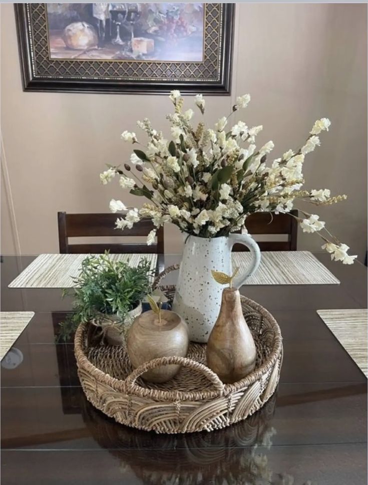 a table with flowers and vases on it in a basket next to a painting