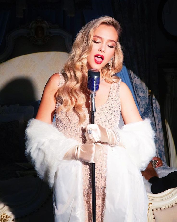 a woman in a white dress singing into a microphone with her hands folded over her chest