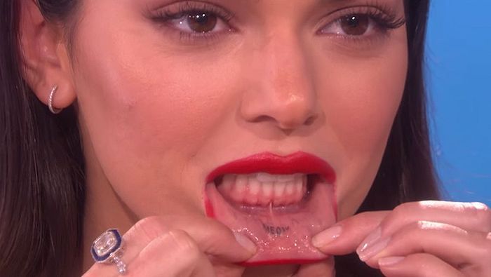 a close up of a person with red lipstick and piercings on her tongue, holding something in her mouth