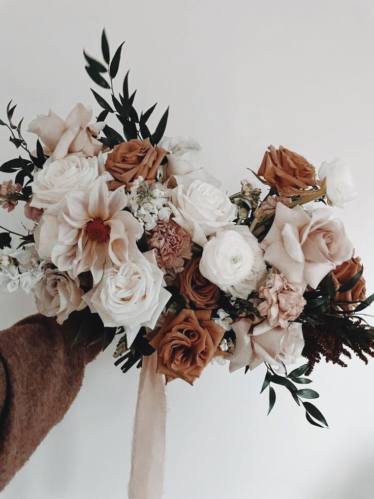 a bridal bouquet is being held up by someone's hand with a brown sweater on it