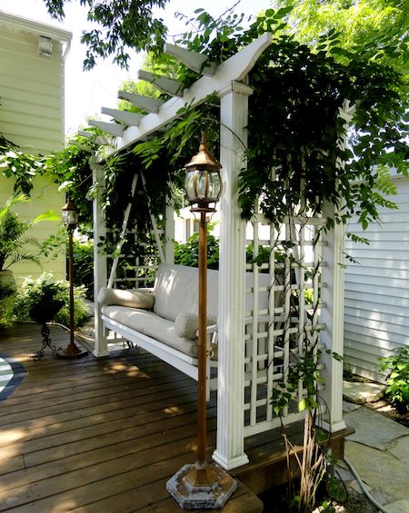 a white bench sitting on top of a wooden deck next to a lush green tree