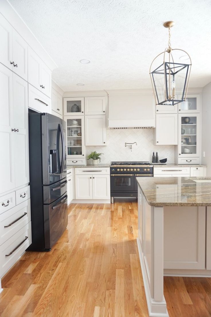 a large kitchen with white cabinets and black refrigerator freezer next to wooden flooring