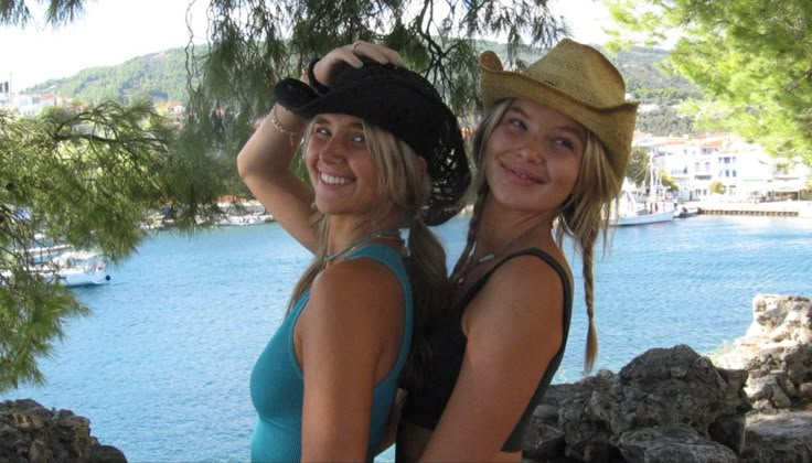 two women standing next to each other in front of a body of water and trees