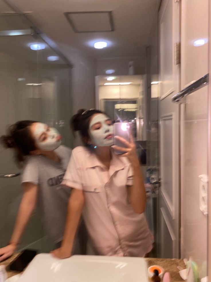 two people are in the bathroom with their faces painted white and one person is taking a selfie