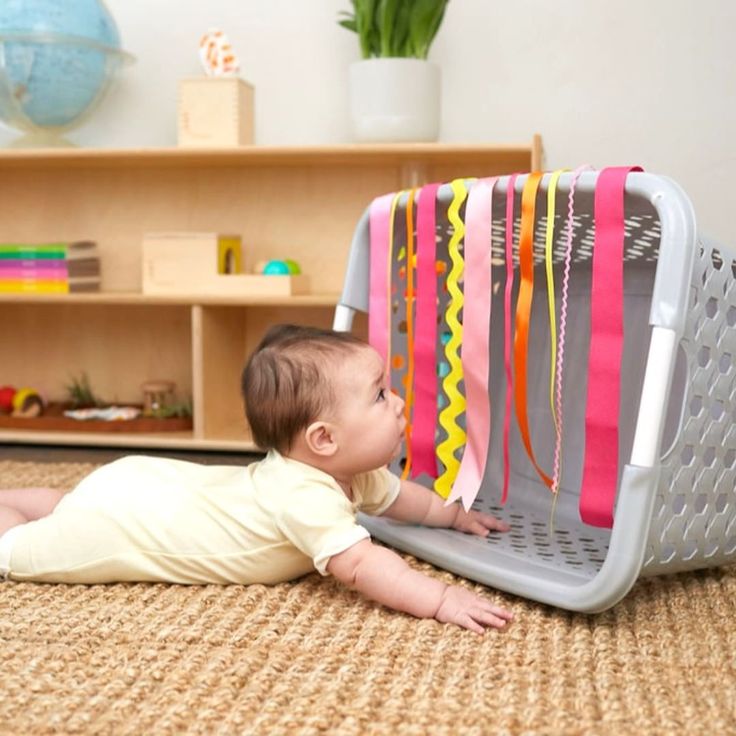 a baby laying on the floor next to a rack with ribbons hanging from it's sides