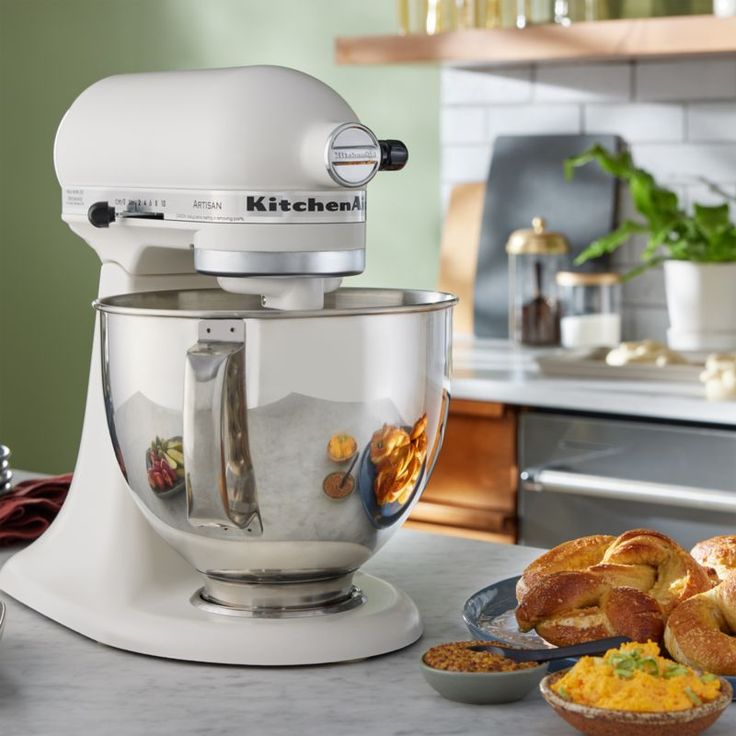 a white kitchen mixer sitting on top of a counter next to some bread and other food