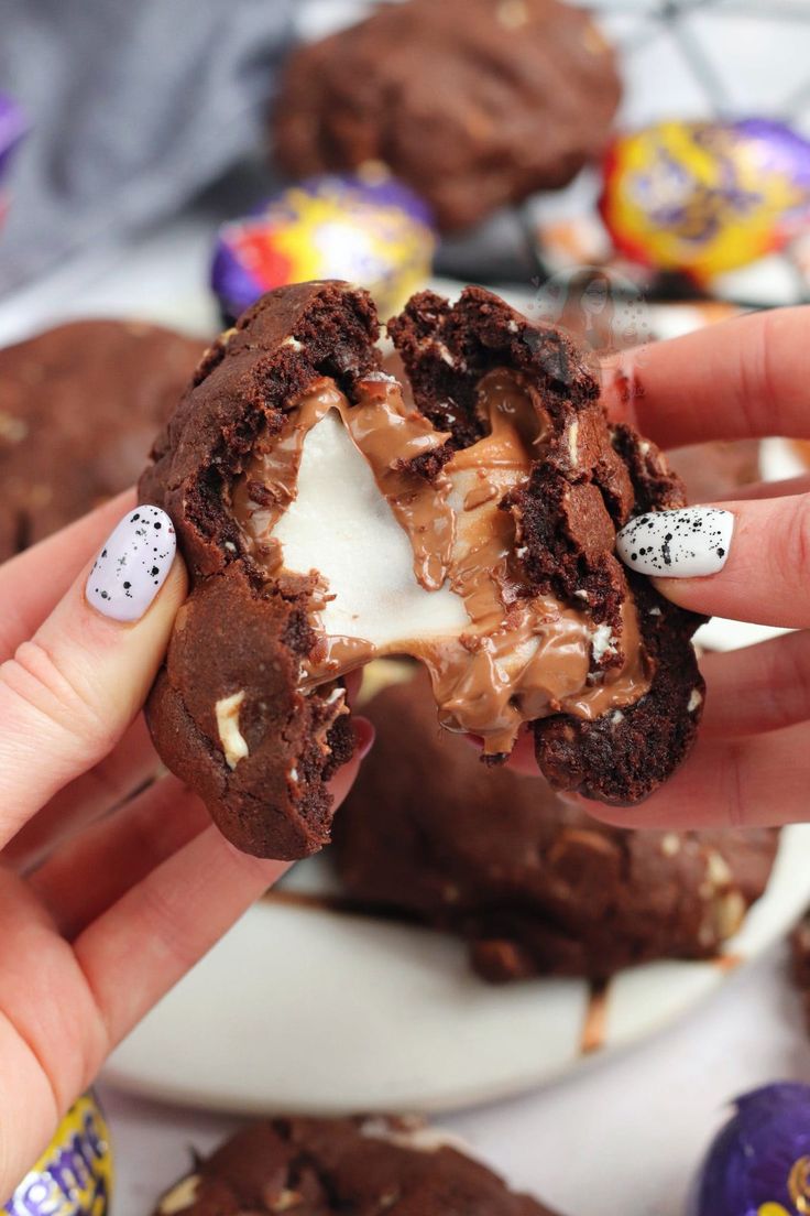 a person holding a chocolate cookie with white frosting